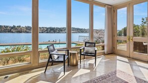 A spacious balcony with large windows overlooking a lake and a pool. - Stunning Waterfront Mansion w Pool n Hottub (Mercer Island)