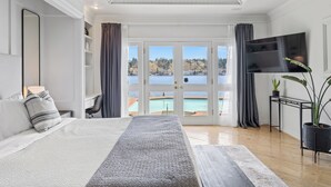 A bedroom with a large bed, a TV, a plant, and a view of a pool and mountains. - Stunning Waterfront Mansion w Pool n Hottub (Mercer Island)