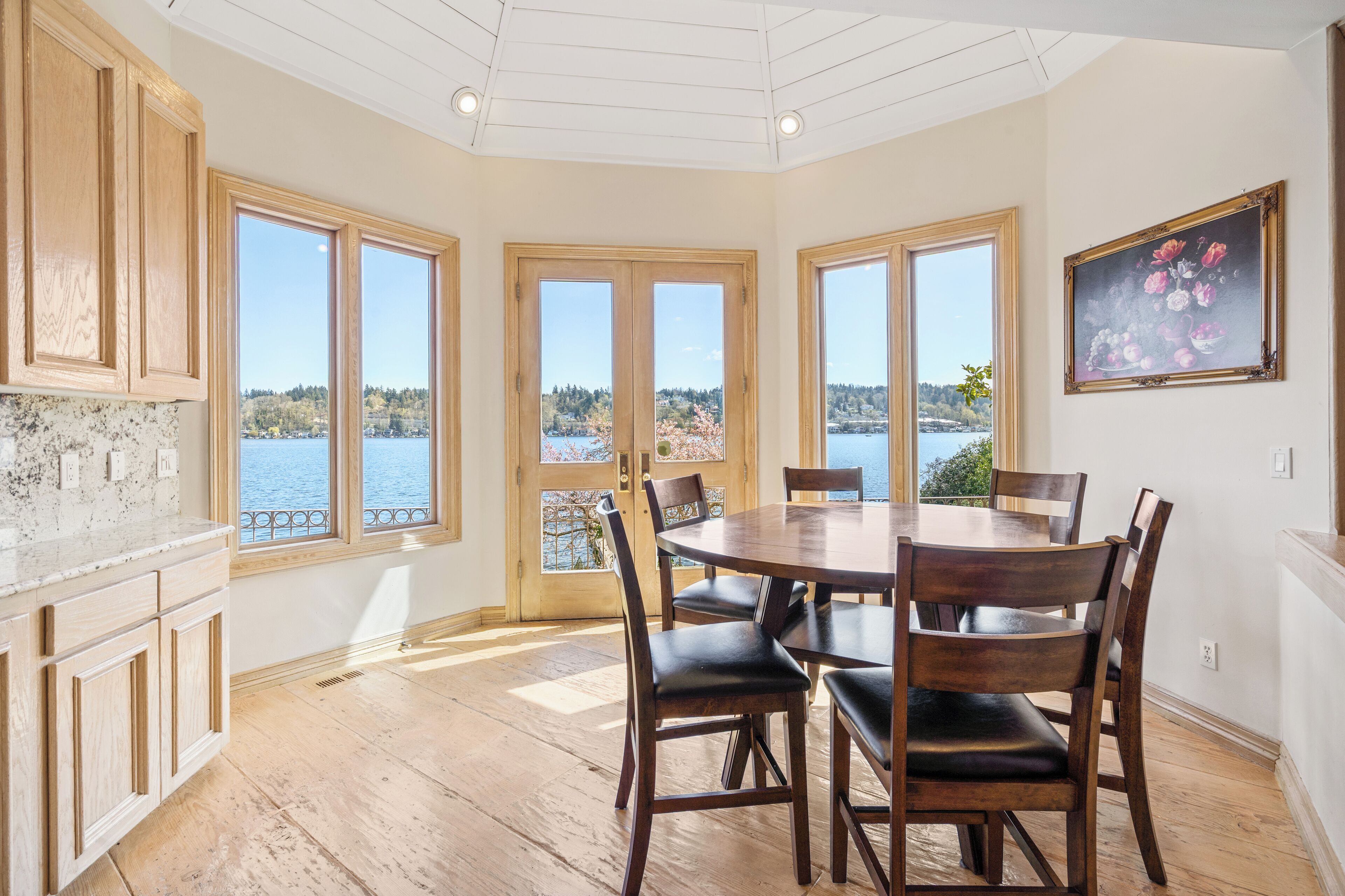 Un comedor con una mesa grande y sillas, armarios de madera y ventanas amplias con vista a un lago.