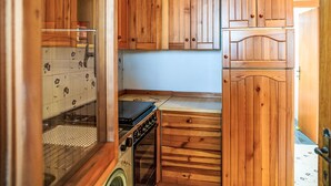 Une cuisine de taille réduite, avec des meubles de rangement en bois, un lave-linge et un petit plan de travail.