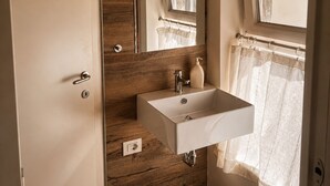 A bathroom with a wooden wall, a white sink, a mirror, and a window with a curtain. - Borgovivo Loft B Modern Loft Bergamo City Center (Bergamo)