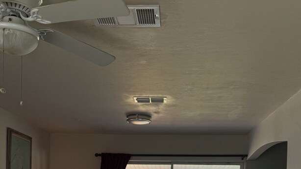 Una sala de estar con un sofá, una mesa de comedor con sillas, un ventilador de techo y vistas a una masa de agua a través de un ventanal.