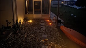Una casa moderna con un patio que tiene un sendero de grava, iluminación exterior y un pequeño jardín.