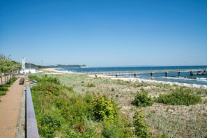 A coastal walkway with a beach, a pier, and a building in the background. - Small but nice vacation home near the beach - Tiny Home No. 822 - Tiny (Göhren)