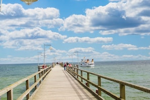 A wooden pier extending into calm waters with a boat in the distance and a clear sky above.