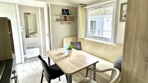 A compact living space with a dining table, chairs, a sofa, a window with a view, and a small shelf with decorative items.