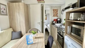 A compact kitchenette with a microwave, oven, and coffee maker, a small dining area with a table and chairs, and a bed in the background.