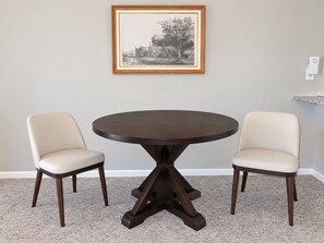 A dining table with a dark wood finish and a central pedestal base, flanked by two upholstered chairs with a light fabric. - Recreation Central ILM (Wilmington)