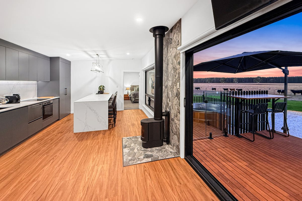 A modern kitchen with a central island, a built-in stove, and a dining area with a view of a farm.