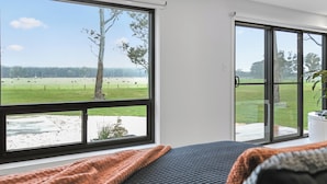 A bedroom with a large window offering a view of a grassy field and trees. - Warrawindi Escapes (Penola)