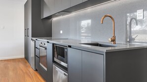 A modern kitchen with stainless steel appliances, a built-in oven, microwave, and dishwasher, and a copper faucet. - Warrawindi Escapes (Penola)