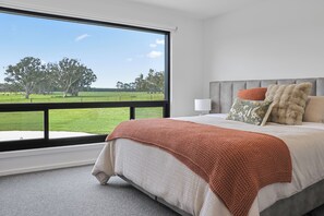 A bedroom with a large window, a bed with a grey headboard, and a view of a green field. - Warrawindi Escapes (Penola)