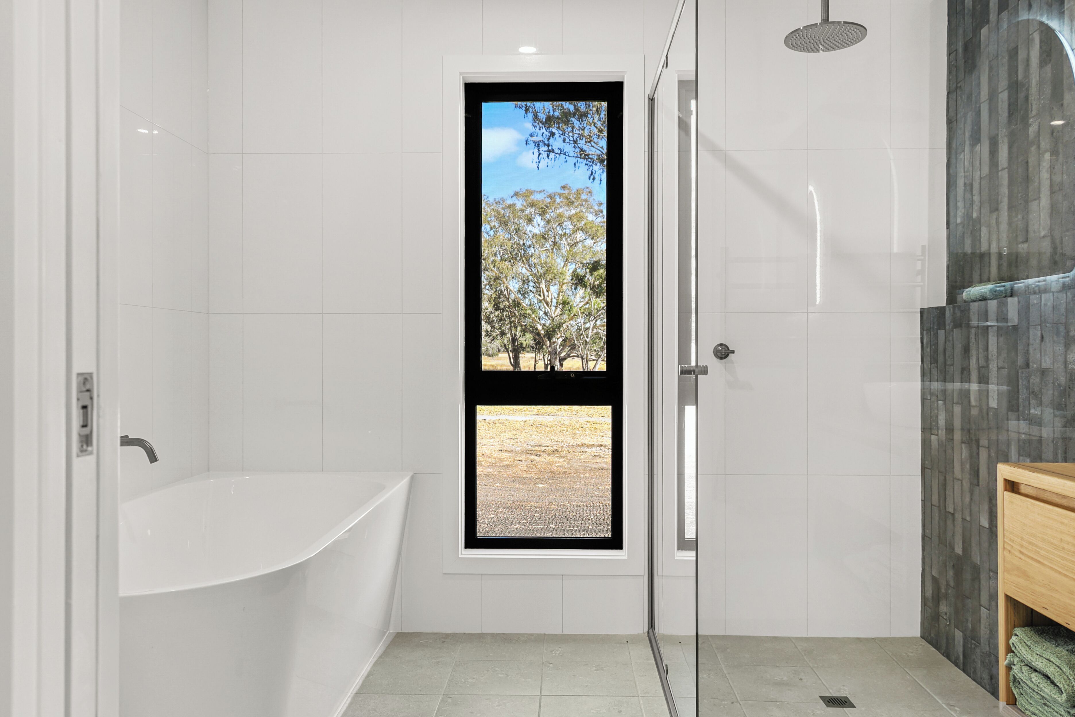 Une salle de bain moderne avec une baignoire sur pieds, une douche à parois de verre et une vue sur les arbres par une porte.