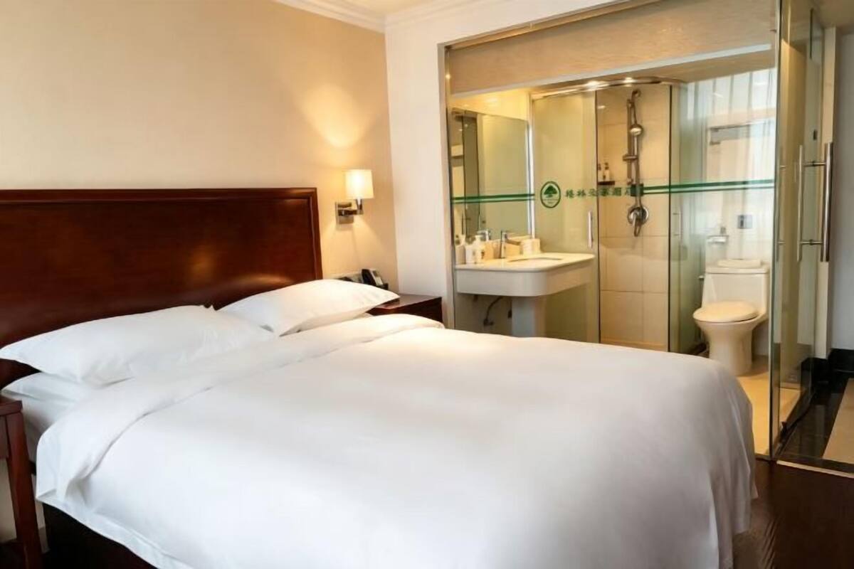 A hotel room with a large bed, a bedside table, a mirror, a sink, and a shower.
