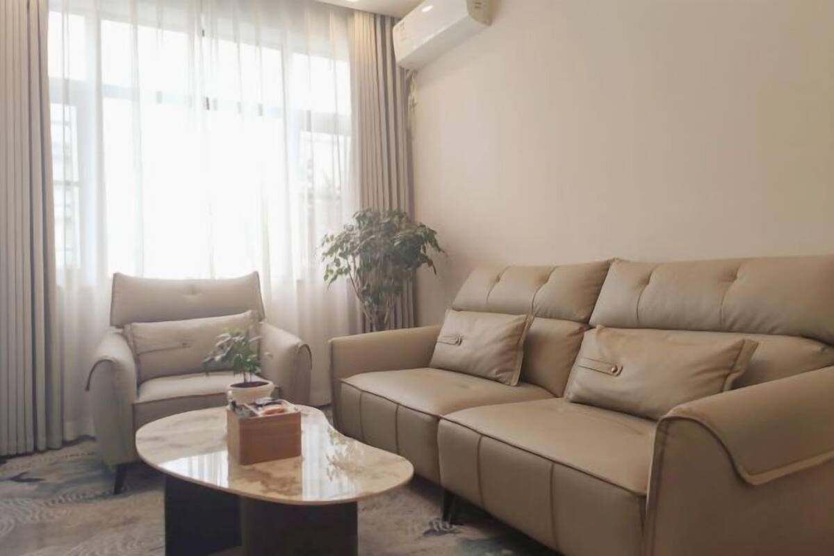 A living room with a beige sofa, a round coffee table, and a potted plant.