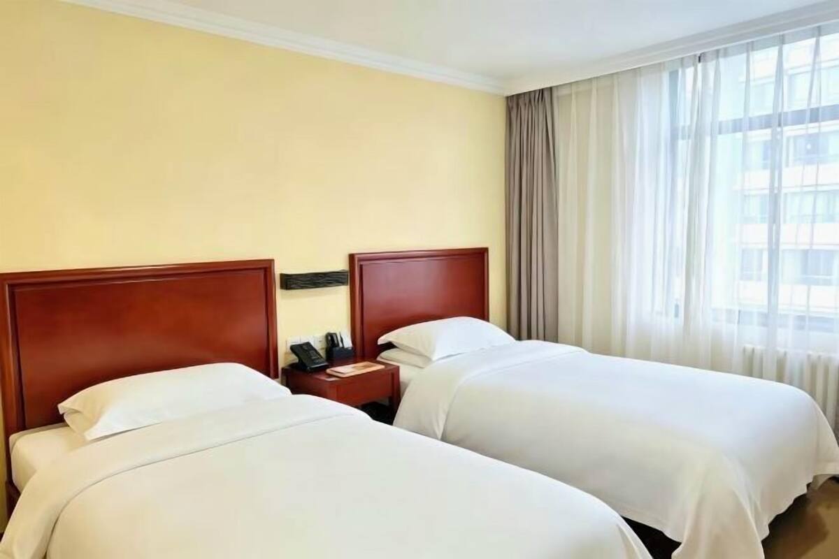 A hotel room with two beds, a nightstand, and a window with curtains.