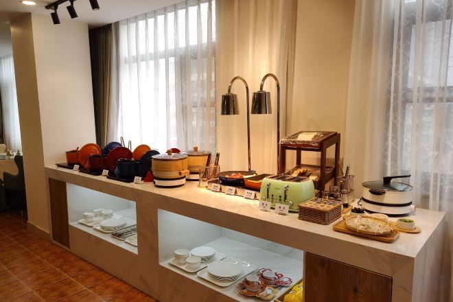 A buffet setup with various food items and containers, a lamp, and a window with curtains.