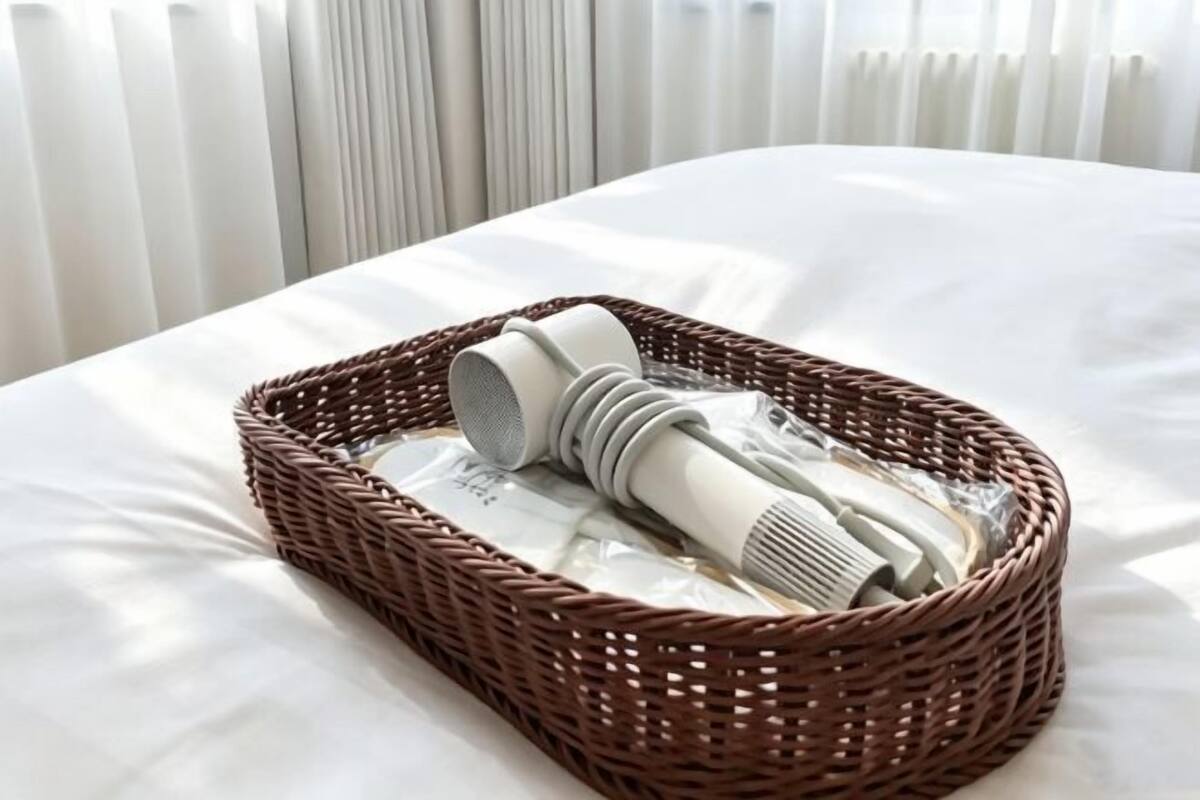 A wicker basket with a hairdryer and a rolled-up towel on a bed with white sheets.
