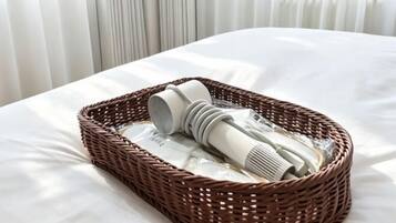 A wicker basket with a hairdryer and a rolled-up towel on a bed with white sheets.