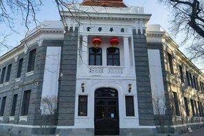 Un bâtiment de style classique, doté d’une façade symétrique, d’une entrée centrale avec une porte noire et de deux lanternes rouges au-dessus de l’entrée.