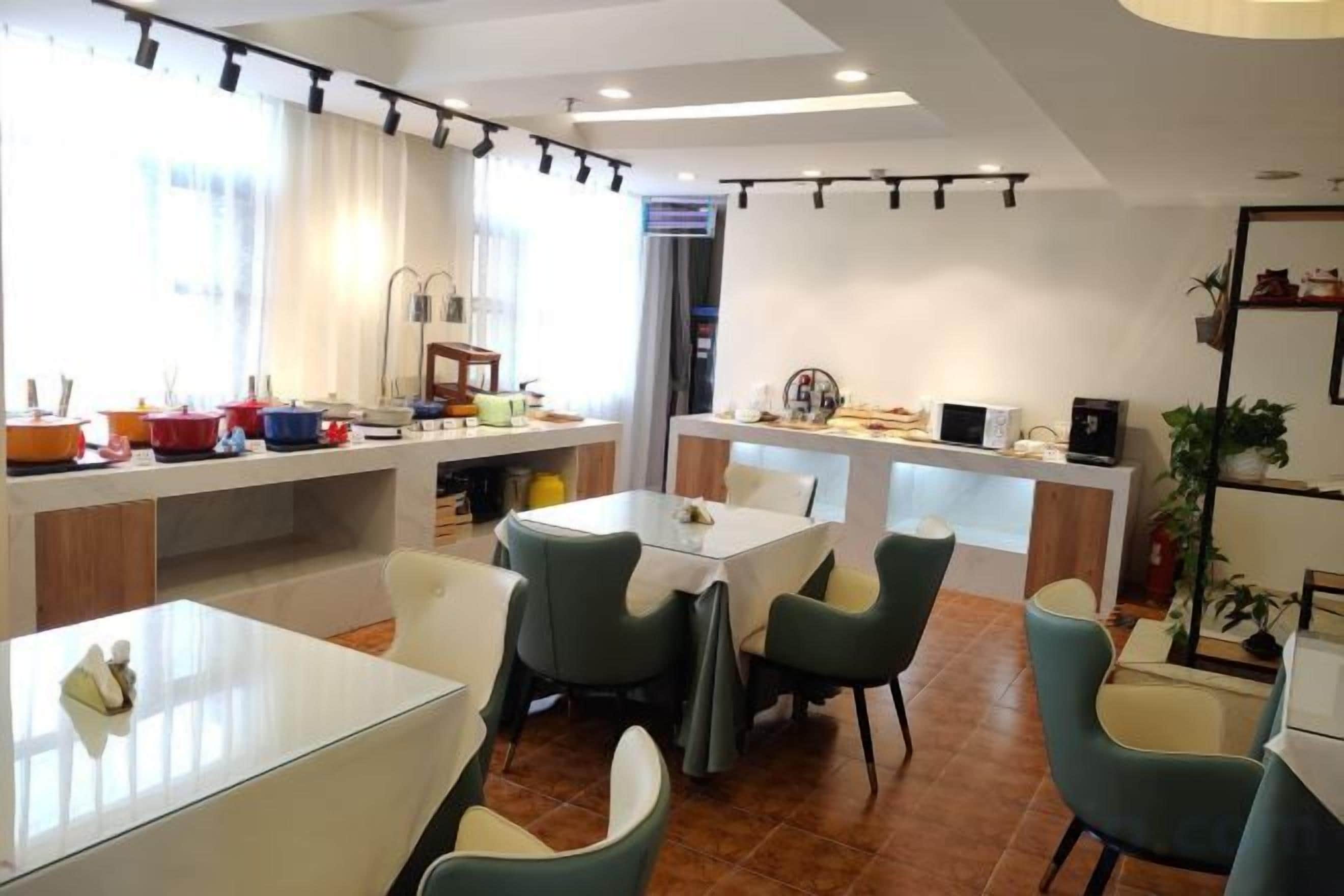 A modern dining area with tables and chairs, a kitchen in the background, and a large window providing natural light.