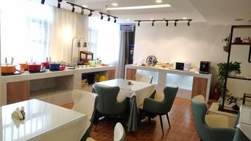 A modern dining area with tables and chairs, a kitchen in the background, and a large window providing natural light.