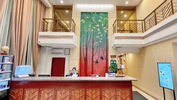 A hotel reception area with a red reception desk, a large vertical mural, a staircase, and a digital information board.