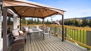 Een houten terras met een overdekte zithoek, een buitentafel en stoelen.