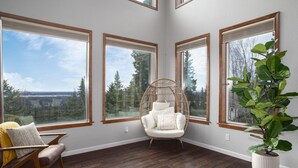 A room with large windows, a hanging chair, a potted plant, and a wooden floor.