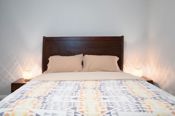 A bed with a wooden headboard, two beige pillows, and a patterned bedspread. There are two bedside lamps on either side of the bed.