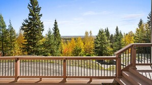 A wooden deck with a railing overlooking a forested area with autumn foliage.