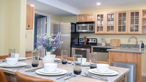 A modern kitchen with wooden cabinets, stainless steel appliances, and a dining area set for four.