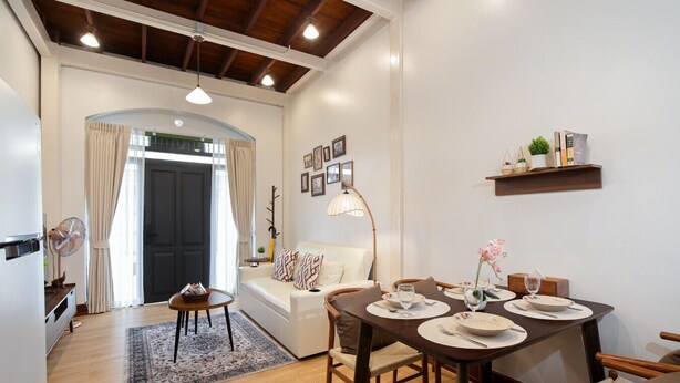 Een moderne woonkamer met een eethoek, met een bank, een eettafel gedekt voor twee personen, en een klein bijzettafeltje met een lamp.