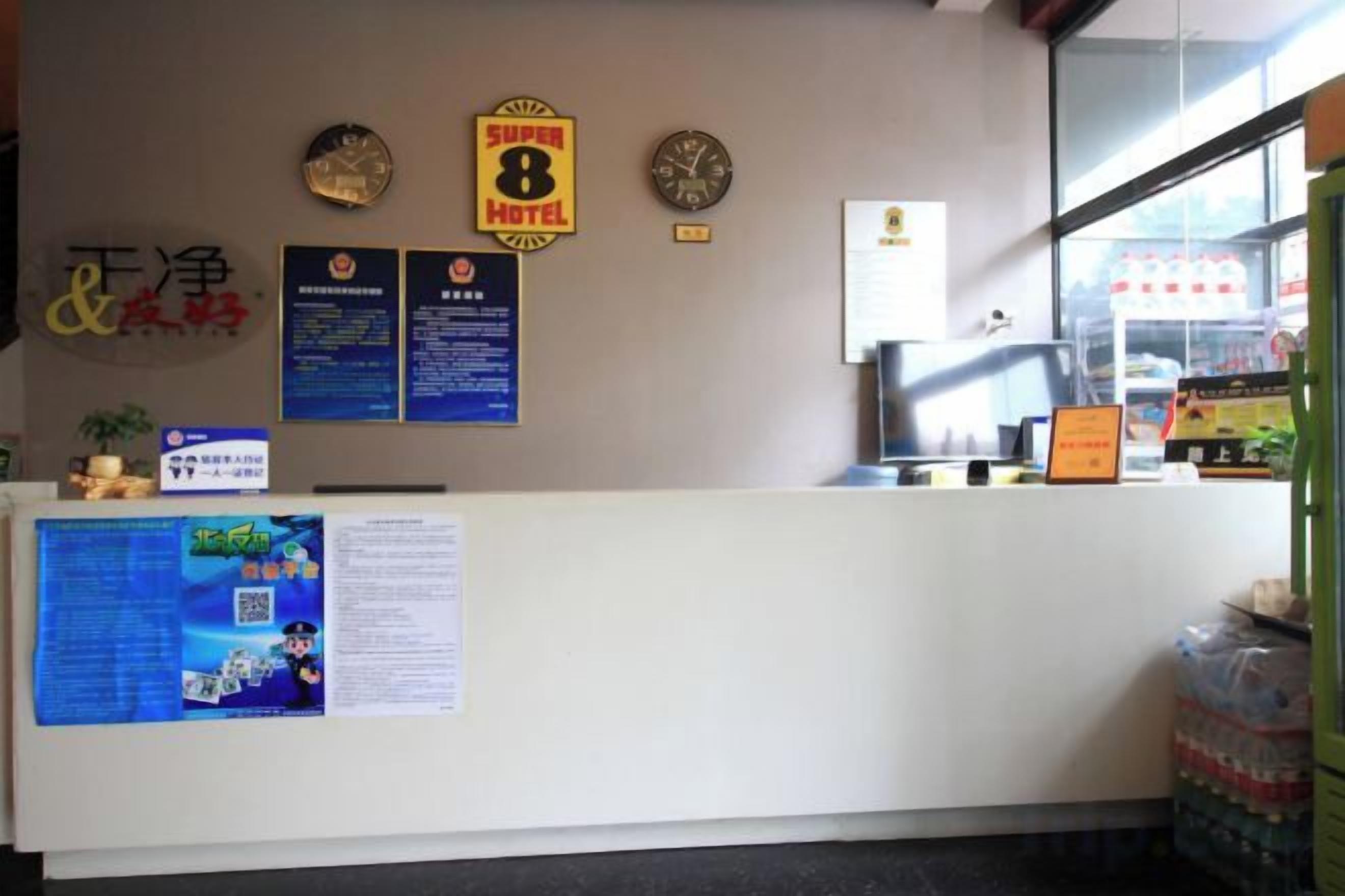A hotel reception desk with a bulletin board, a clock, and a window with a view of the outside.