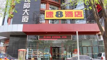 Un hotel con un letrero llamativo que dice '速8酒店' y un número de contacto exhibido debajo de la entrada.