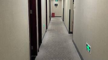 Un pasillo de hotel con puertas a ambos lados, una alfombra estampada y una señalización de salida de emergencia verde.