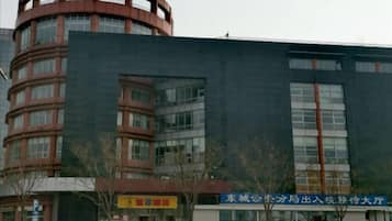 Un edificio de varios pisos con una estructura cilíndrica destacada a la izquierda, una entrada amplia con un letrero, y un estacionamiento al frente.