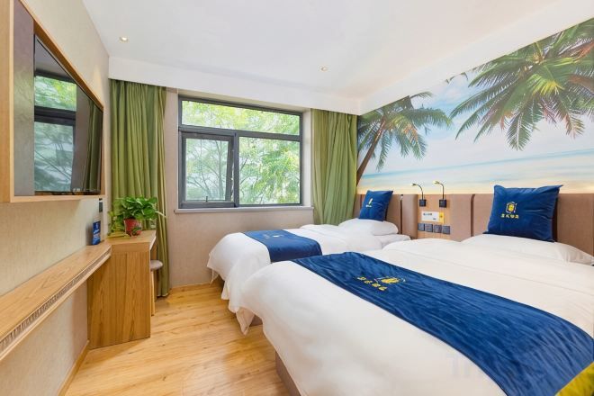 Habitación de hotel con dos camas, un escritorio, una silla, un ventanal con cortinas y un mural en la pared.