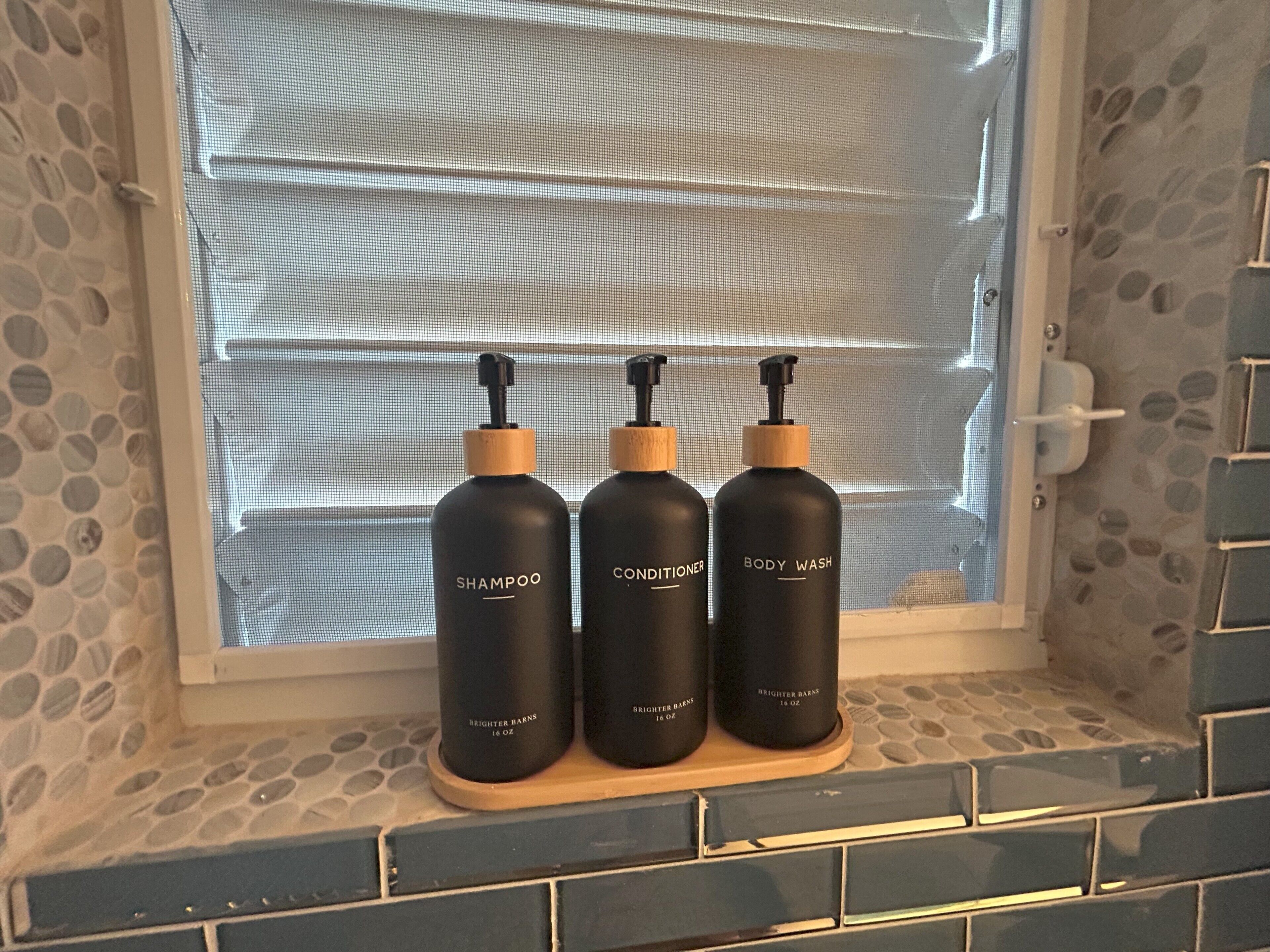 Drei Flaschen Brightner Barns Duschgel und Conditioner auf einem Regal neben einem Fenster mit strukturierter Wand.
