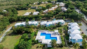 An aerial view of a resort with multiple bungalow-style buildings, a central swimming pool, and lush greenery surrounding the property. - NEW! Saltwater Serenity - Poolside & Walk to Beach (Christiansted)