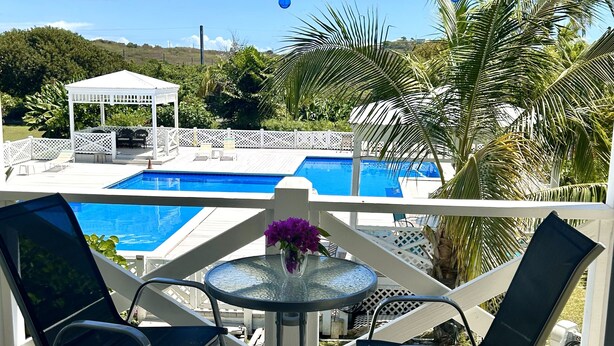 A covered outdoor area with a pool, lounge chairs, and a table with a vase. - NEW! Saltwater Serenity - Poolside & Walk to Beach (Christiansted)