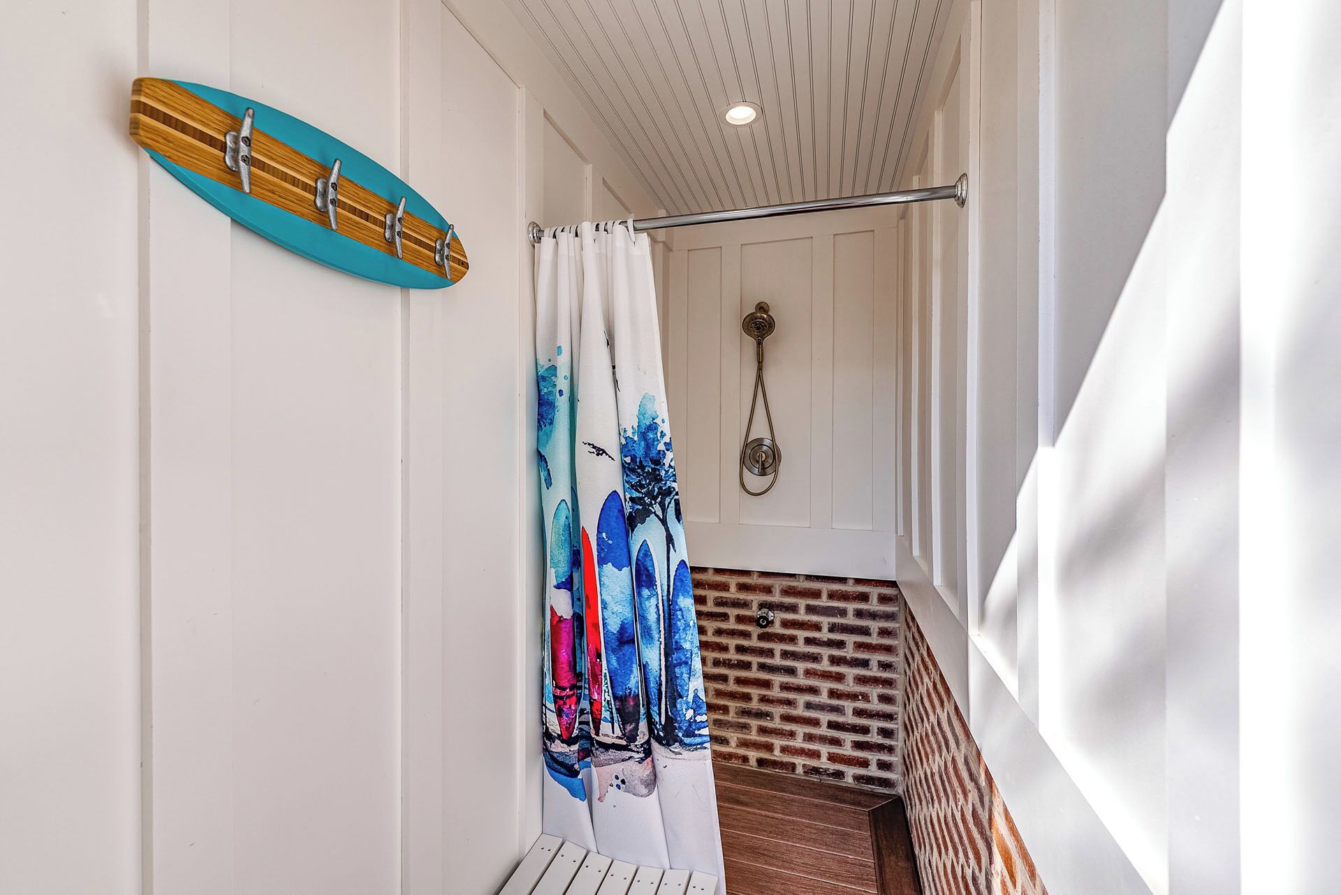 A staircase with a brick wall and a white door with a shower curtain featuring a blue and red abstract design.