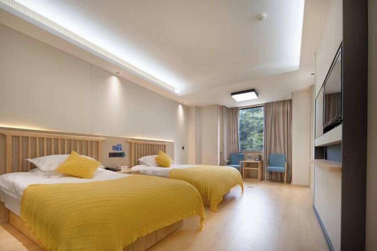 A hotel room with two beds, a TV, a small table, and a window with curtains.