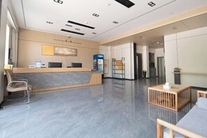 Una recepción moderna con un mostrador de mármol, una zona de estar con una mesa de centro de madera y una máquina expendedora.