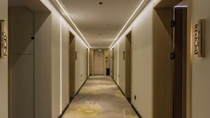Pasillo de hotel con alfombra de motivos florales, puertas con números de habitación e iluminación empotrada en el techo.