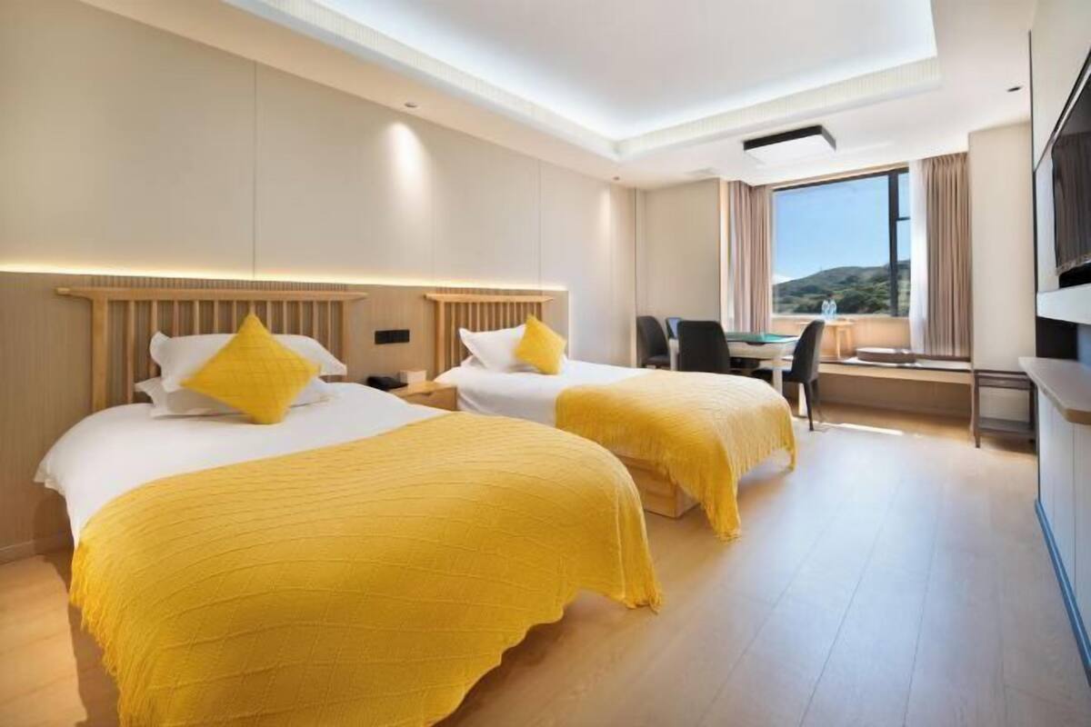 A hotel room with two beds, a desk, a chair, and a TV.