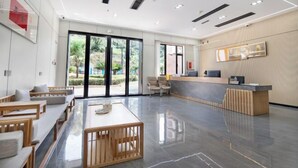 Un vestíbulo amplio con mostrador de recepción, zona de estar y grandes puertas de vidrio que dan a un jardín exterior.