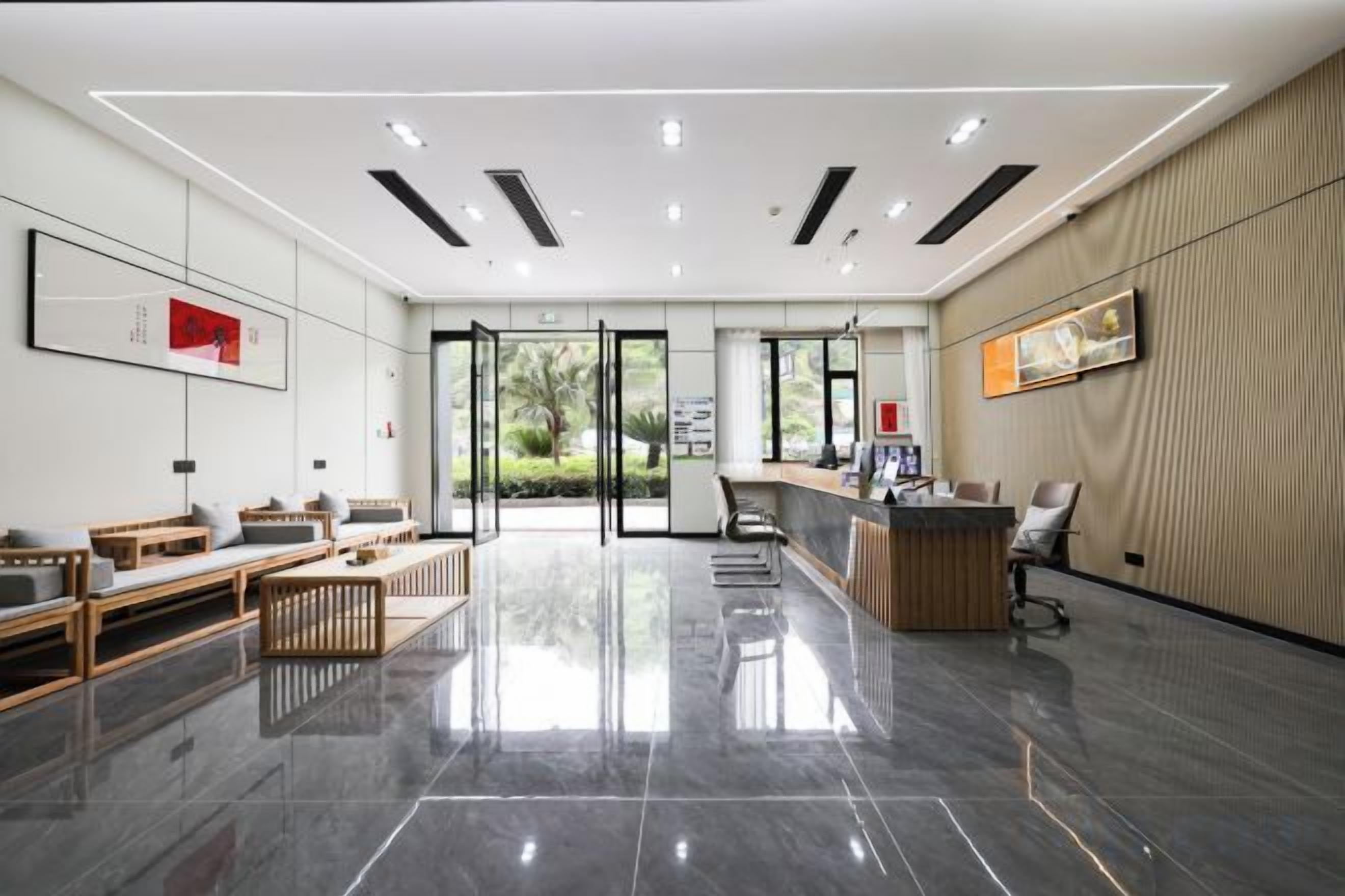 Un área de recepción moderna con mostrador, zona de estar y vistas a través de puertas de vidrio.