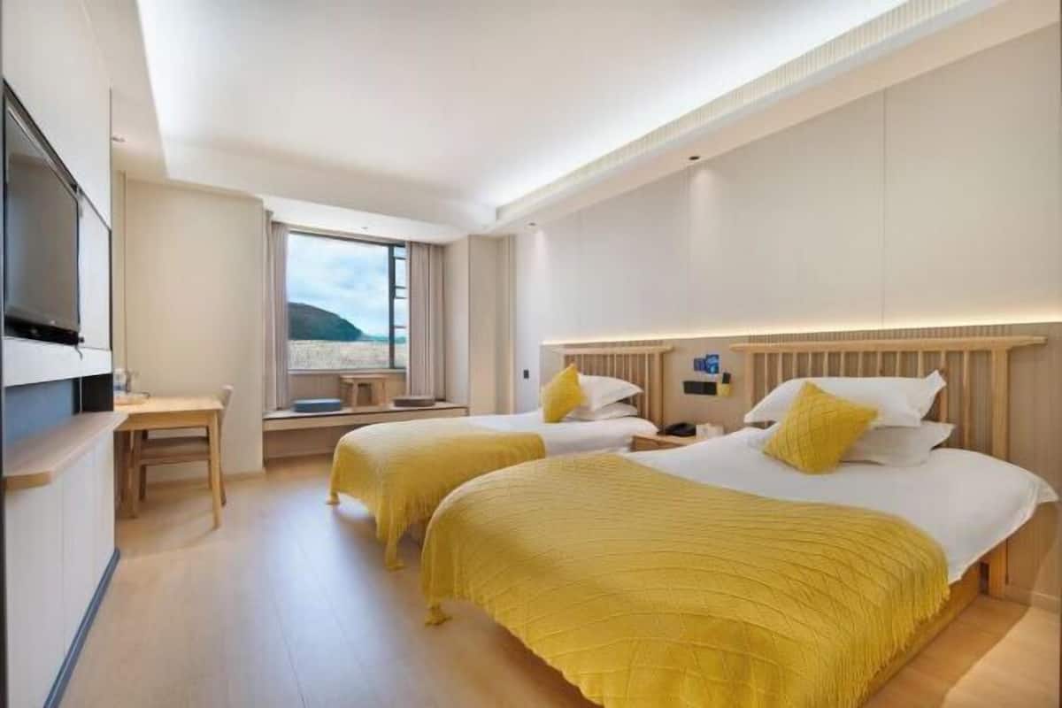 A hotel room with two beds, a TV, a desk, and a window with a view of the beach.