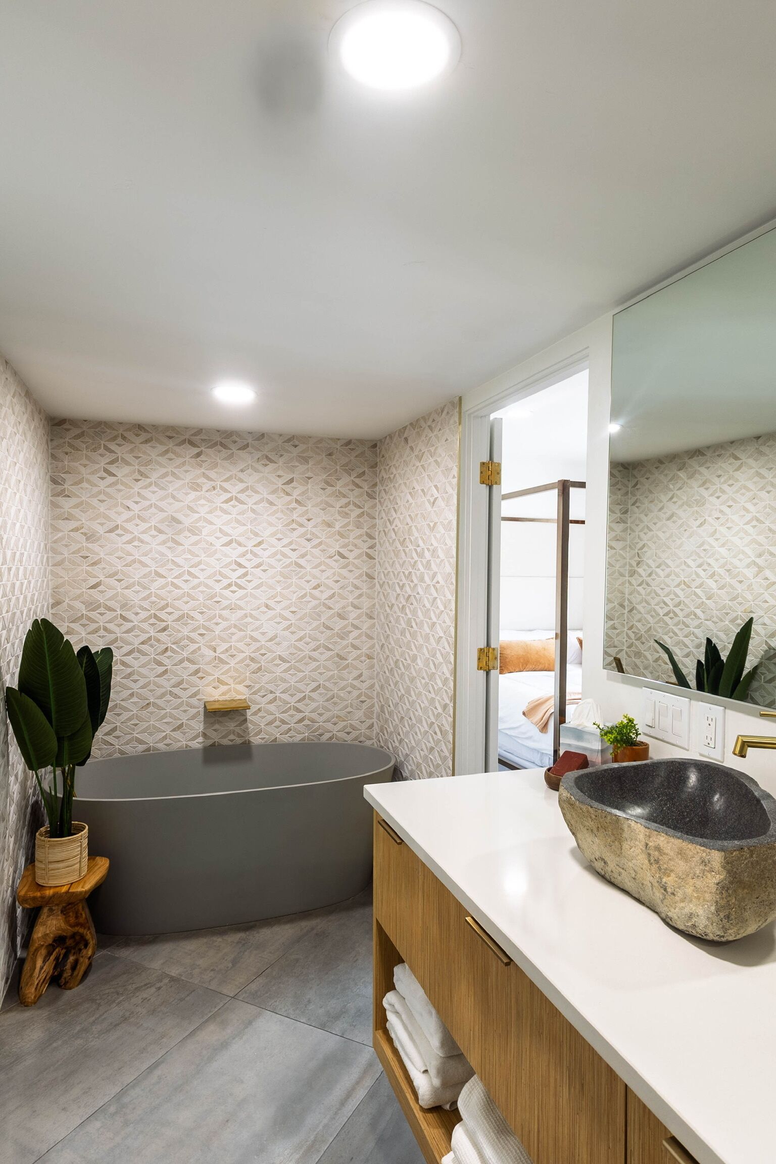 Un baño moderno con una bañera independiente, un espejo grande y un tocador de madera con lavabo de piedra.
